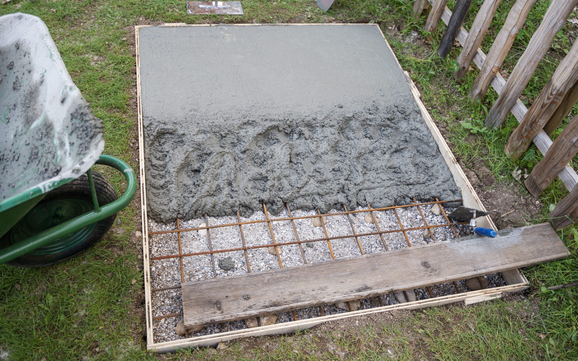 Hole in a ground in backyard, framed with wooden boards, filled with fresh cement about to be leveled.
